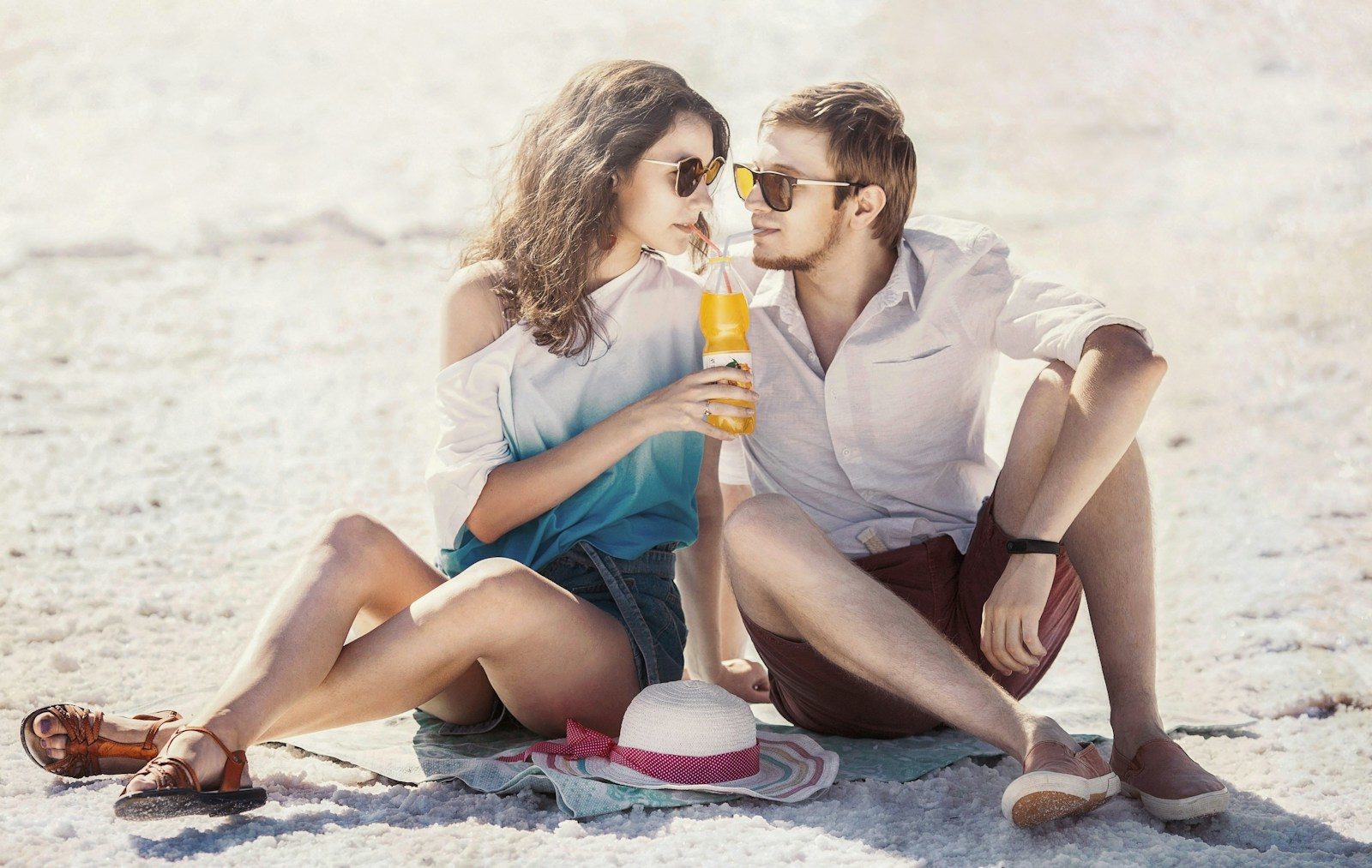 un homme et une femme assis sur la plage en train de boire du jus d'orange